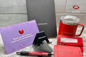 Branded promotional items including notebook, mug, pen, and cardholder displayed at a corporate exhibition event.
